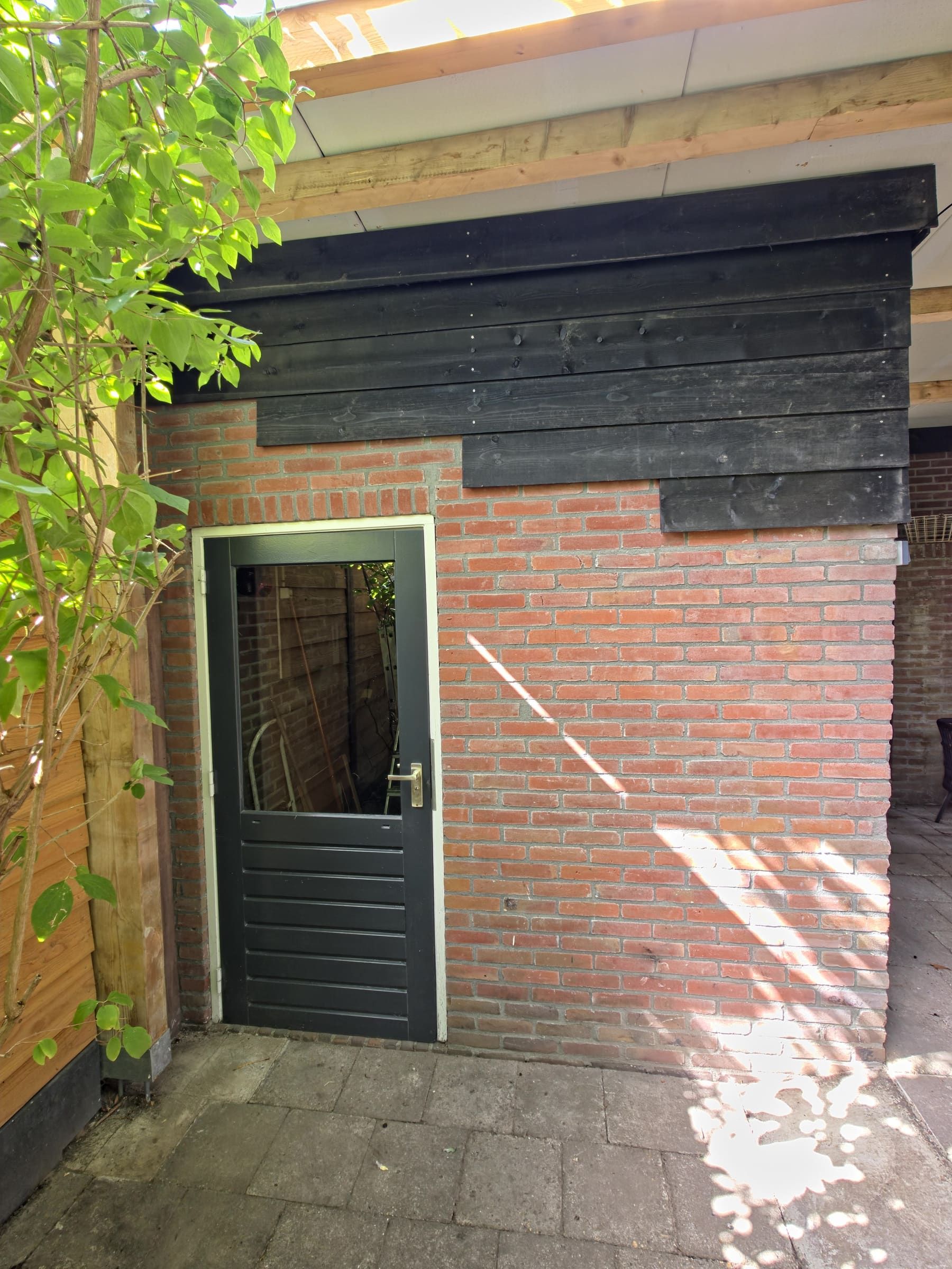 Berging onder de overkapping, met de grijze deur in het metselwerk